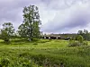 Et lite hus står i en grønn eng med trær og skyet himmel i bakgrunnen.