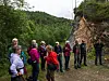 En gruppe turgåere står på en sti ved en bratt fjellvegg og skogkledd landskap.
