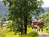 Turgåere går langs en grusvei ved en rød gårdsbygning i et grønt landskap.