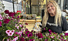Kvinne står ved et utendørs blomsterbord med rosa og lilla blomster foran et skilt som leser Hagemagasinet.