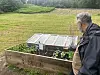 Mann ved en opphøyet kjøkkenhage med små planter, i et grønt hageområde.