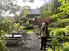 Gult hus omgitt av hage, trær, busker og flere piknikbord på en gruslagt uteplass.