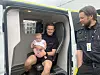 En mann med et barn sitter i bakrommet på en ambulanse mens en uniformert ansatt står ved døren.