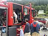 Barn og voksne står ved en åpen rød brannbil på en parkeringsplass med andre kjøretøy i bakgrunnen.