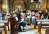 Kor synger i en kirke mens en pianist sitter ved flygelet foran sangerne.