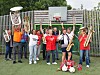 Et brassband står samlet utendørs foran en basketballkurv og holder instrumentene sine.