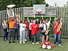 Et brassband står samlet utendørs foran en basketballkurv og holder instrumentene sine.