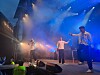 Tre personer opptrer på en scene med blå lys og røyk under en utendørskonsert.