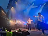 Tre personer opptrer på en scene med blå lys og røyk under en utendørskonsert.