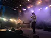 To artister på en scene med røyk, lysrigg og høyttalere under en innendørs konsert.