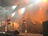 Band opptrer på scene med gitarer, mikrofoner og oransje scenelys.