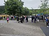 Løpere og tilskuere på en brosteinsplass omgitt av trær i en park.