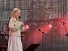 En sanger står på en scene med mikrofon foran et sort bakteppe med SpareBank 1 Nordmøre-logo. Rødt lys.