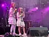 To unge sangere står på en scene med mikrofoner og lilla scenelys.