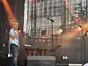 Ung person står med mikrofon på en scene med lys og utstyr i bakgrunnen.