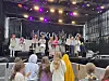 Gruppe unge artister på scene foran publikum under lilla og gule scenelys.