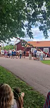 Folk står samlet ved en rødmalt bygning mens en dekorert trekonstruksjon løftes utendørs.