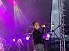 Artist synger med mikrofon på en scene badet i lilla lys.