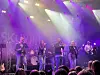 Et band opptrer på en scene med lilla og hvite scenelys foran publikum.