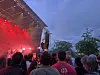 Publikum foran en utendørsscene med rødt scenelys i skumringen.