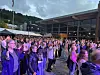 Mange mennesker står samlet utendørs foran en arena i kveldslys.
