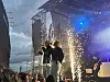 Band opptrer på scene med gnister, røyk og blått lys under en utendørskonsert.