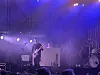 Musiker spiller gitar på en scene med blå og lilla scenelys og røyk.