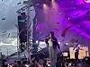 Musiker opptrer på en stor utendørsscene med konfetti i luften og lilla lys.