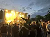 Publikum foran en opplyst utendørsscene med sterke lys og pyroteknikk i bakgrunnen.