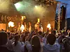 Publikum foran en utendørsscene med lys, røyk og flammer under en konsert.
