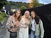 Tre kvinner står sammen og smiler utendørs ved et arrangement.
