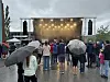 Folk (noen med paraplyer) står foran en lysbelyst utendørsscene i regnvær.
