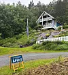 Lite hus på en grønn ås med hvitt gjerde og et åpent-skilt i forgrunnen.