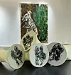 Hvite skulpturelle former med svarte blomstertegninger foran et stort kunstverk i et lyst rom.