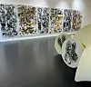 Svart-hvite kunsttrykk med gullfarger utstilt langs en vegg i et lyst gallerirom.