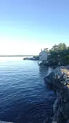 Steinete kyst med en liten sjøbu ved vannet under en klar himmel.
