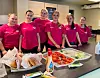 Seks kvinner står bak en benk med hamburgere i en kantine eller kiosk.