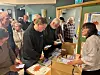 Personer står rundt et bord med esker med bøker i i et rom med grå vegger.
