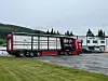 Rød semitrailer parkert foran industribygg på en våt grusplass.