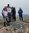 Fire turgåere med turstaver står på en steinete fjellknaus i tåke.