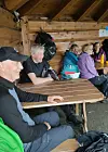 Flere eldre personer sitter ved et trebord inne i en rustikk trehytte.