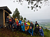 En gruppe turgåere står samlet ved en hytte med utsikt over skogkledd landskap og dal.