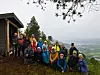 En gruppe turgåere står samlet ved en hytte med utsikt over skogkledd landskap og dal.