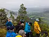 Turgåere i fargerike jakker står på en fjellknaus med utsikt over et grønt dalføre.