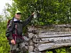 En turgåer i skogen står ved en stor tømmerstokk og holder opp en vannflaske.
