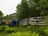 Gruppe vandrere med ryggsekker går ved en steinmur i grønn natur.