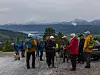 Turgåere med sekker og turstaver står på et utsiktspunkt med fjell og fjord i bakgrunnen.