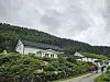Hus med hager ved en vei foran en skogkledd ås under overskyet himmel.