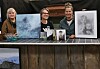 Tre damer bak et bord med utstilte kunstverk, bilder og en innrammet tegning.