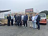 En gruppe personer står foran en byggeplass med en varebil og et bygg under oppføring i bakgrunnen.